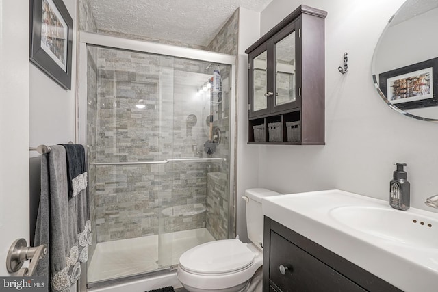 bathroom featuring a textured ceiling, toilet, a shower with shower door, and vanity