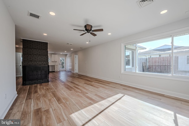 unfurnished living room with ceiling fan, a brick fireplace, a healthy amount of sunlight, and light hardwood / wood-style floors