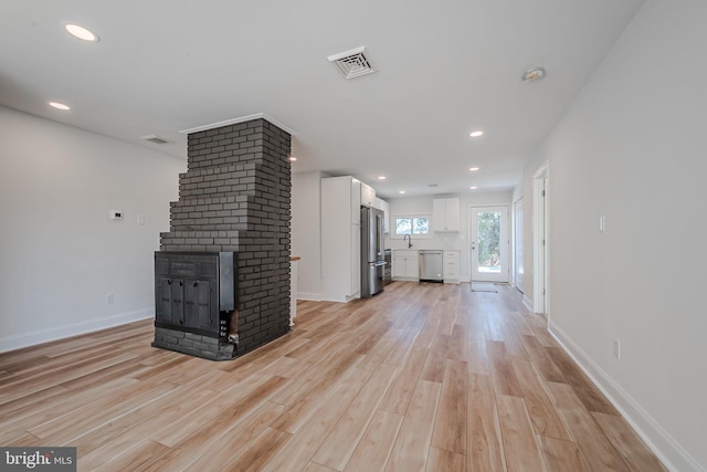 unfurnished living room with sink, a multi sided fireplace, and light wood-type flooring