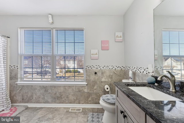 bathroom with tile walls, toilet, vanity, and tile patterned flooring