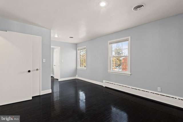 spare room featuring a baseboard heating unit and dark hardwood / wood-style floors