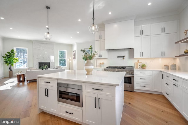 kitchen with white cabinetry, high end range, hanging light fixtures, custom range hood, and a fireplace