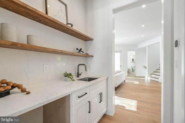 bar featuring sink, white cabinetry, light stone counters, tasteful backsplash, and light hardwood / wood-style floors