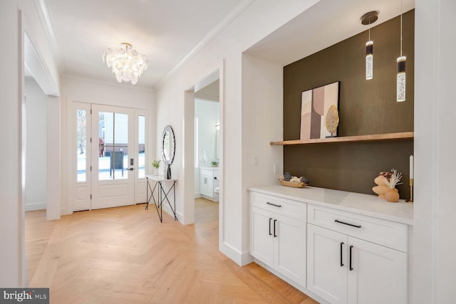 entryway with a notable chandelier, ornamental molding, and light parquet floors