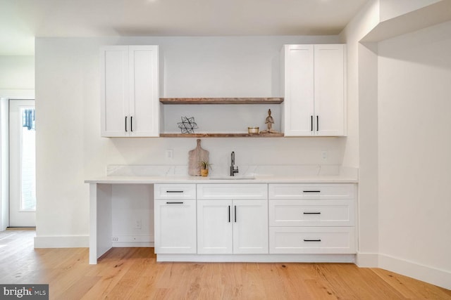 bar with white cabinetry, sink, and light hardwood / wood-style floors