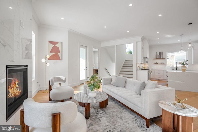 living room featuring a tiled fireplace, sink, ornamental molding, and light hardwood / wood-style floors