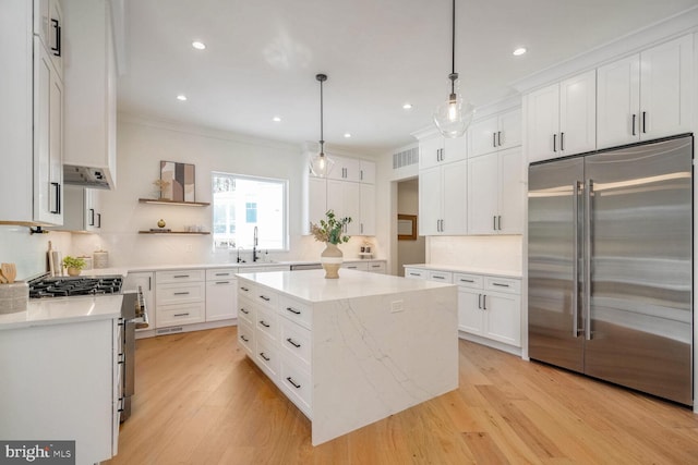 kitchen with ornamental molding, appliances with stainless steel finishes, a kitchen island, pendant lighting, and white cabinets