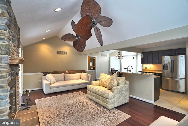 living room featuring a stone fireplace, ceiling fan, dark hardwood / wood-style flooring, vaulted ceiling, and sink