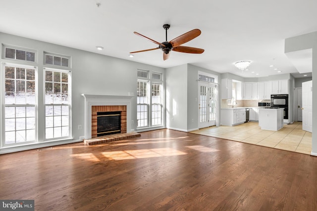 unfurnished living room with ceiling fan, a brick fireplace, sink, and light wood-type flooring