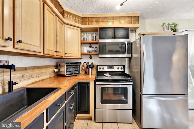 kitchen with open shelves, stainless steel appliances, wooden counters, a sink, and a textured ceiling