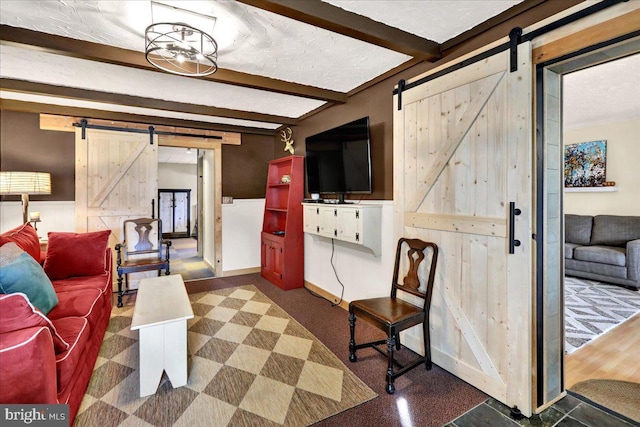 living area featuring beam ceiling, baseboards, and a barn door