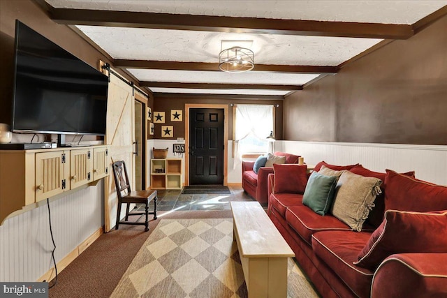 living area featuring beam ceiling, a wainscoted wall, dark carpet, and a barn door