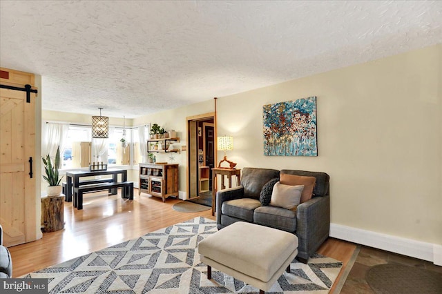 living area with a barn door, a textured ceiling, baseboards, and wood finished floors