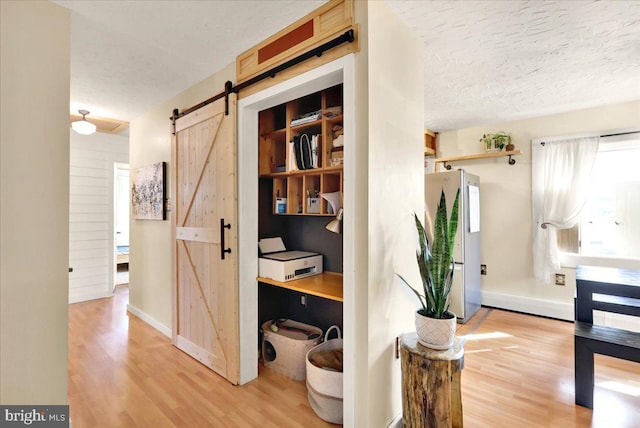 hall featuring a textured ceiling, a barn door, light wood-type flooring, and baseboards