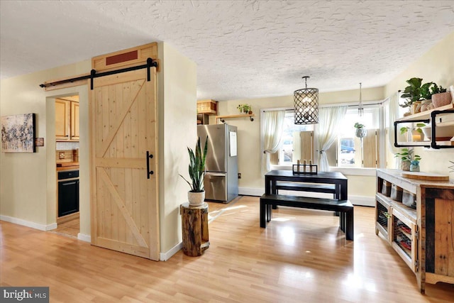 interior space with a textured ceiling, a barn door, light wood-type flooring, and baseboards