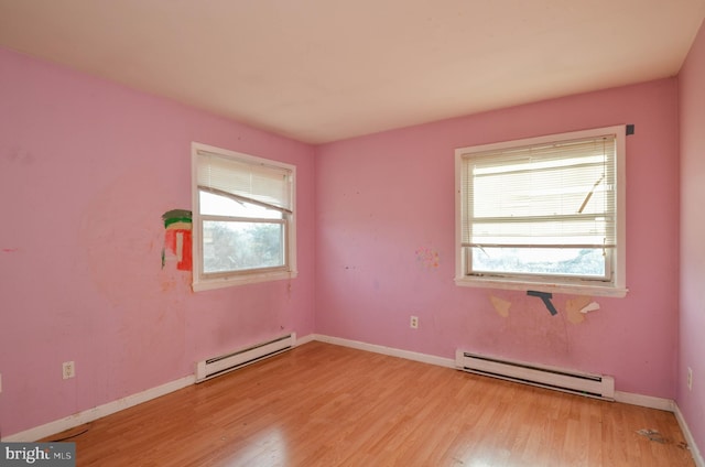 spare room with light hardwood / wood-style floors, a baseboard heating unit, and a healthy amount of sunlight