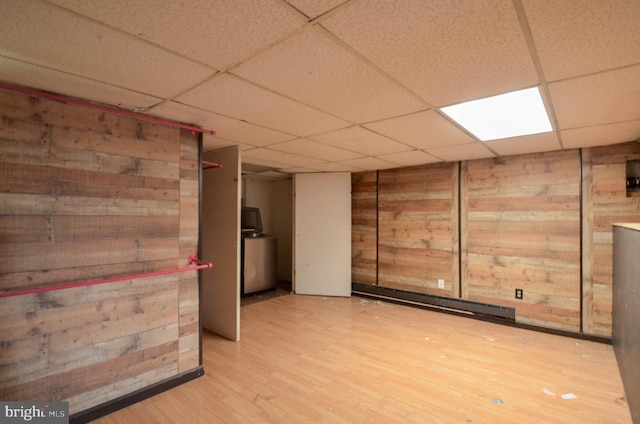 basement featuring light wood-type flooring, washer / dryer, wooden walls, and a drop ceiling