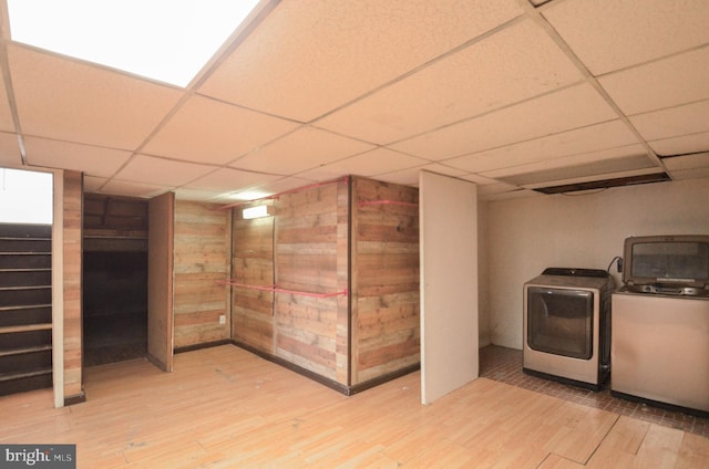 basement with wood walls, washing machine and clothes dryer, a drop ceiling, and light hardwood / wood-style flooring