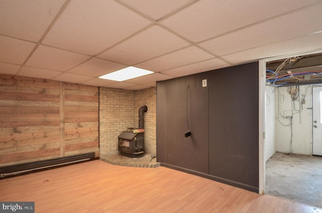 basement with hardwood / wood-style flooring, a baseboard heating unit, a drop ceiling, and a wood stove