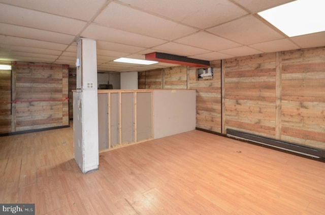 basement with a paneled ceiling, a baseboard radiator, wood walls, and hardwood / wood-style floors