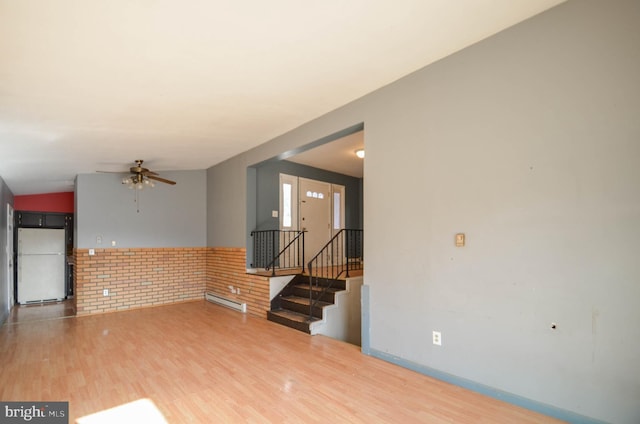 unfurnished living room with hardwood / wood-style flooring, brick wall, ceiling fan, and a baseboard radiator