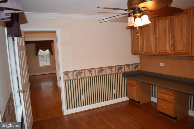 unfurnished office featuring ornamental molding, built in desk, ceiling fan, and dark hardwood / wood-style flooring