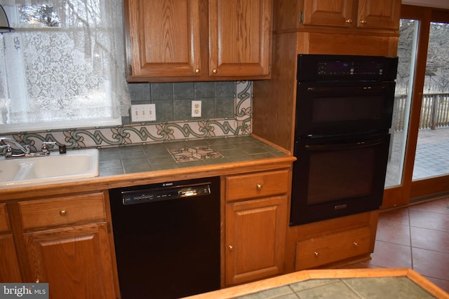 kitchen featuring sink, tile counters, black appliances, light tile patterned flooring, and decorative backsplash