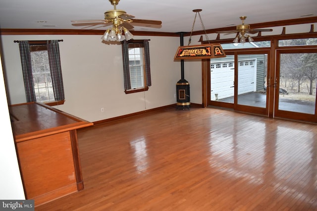 unfurnished living room featuring ceiling fan, ornamental molding, hardwood / wood-style floors, and a wood stove