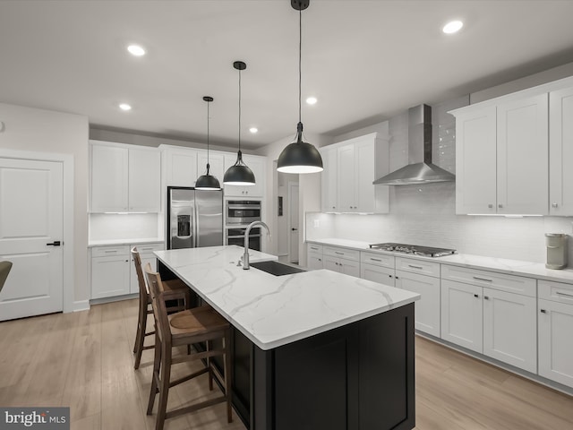 kitchen featuring pendant lighting, white cabinets, a kitchen island with sink, stainless steel appliances, and wall chimney range hood