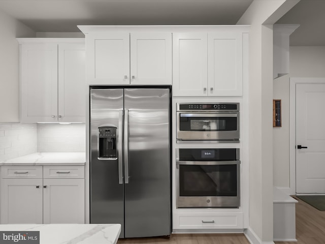 kitchen featuring tasteful backsplash, white cabinets, light stone counters, stainless steel appliances, and light wood-type flooring