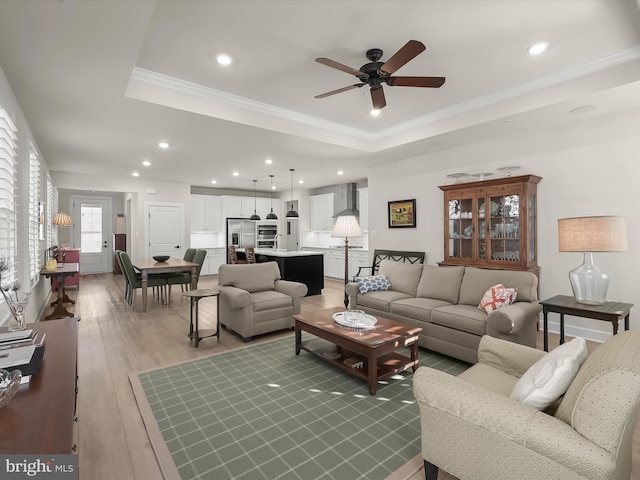 living room featuring ornamental molding, ceiling fan, light wood-type flooring, and a tray ceiling