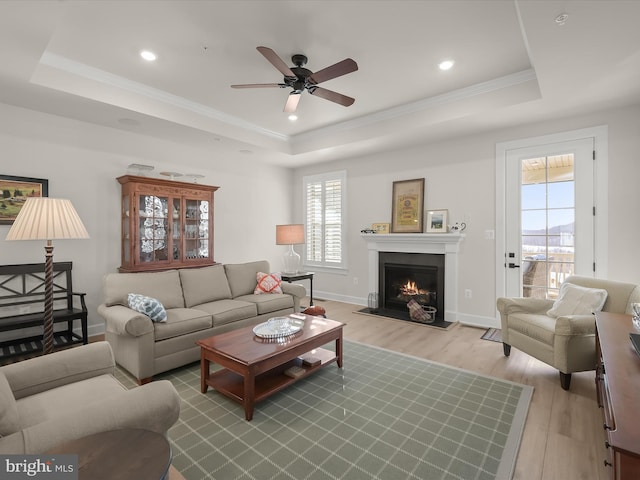 living room featuring crown molding, ceiling fan, a tray ceiling, and light hardwood / wood-style floors