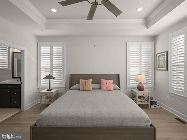 bedroom featuring a raised ceiling, ceiling fan, ensuite bath, and light hardwood / wood-style flooring