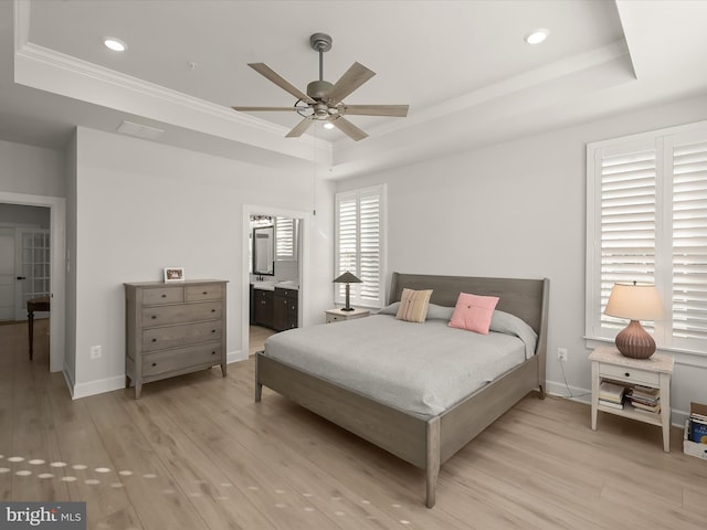 bedroom with a tray ceiling, connected bathroom, light hardwood / wood-style floors, ceiling fan, and crown molding