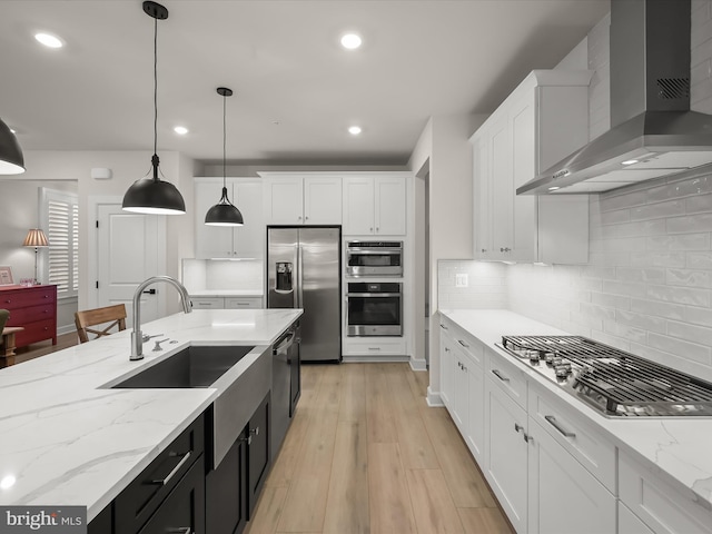 kitchen featuring decorative light fixtures, white cabinets, decorative backsplash, stainless steel appliances, and wall chimney exhaust hood