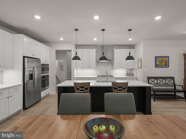 kitchen with pendant lighting, stainless steel appliances, a kitchen island with sink, and backsplash