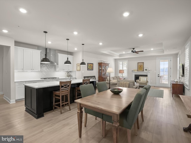 dining space featuring a raised ceiling, ceiling fan, sink, and light hardwood / wood-style floors