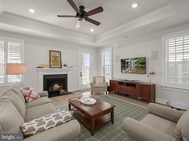 living room featuring crown molding, plenty of natural light, light wood-type flooring, and a tray ceiling