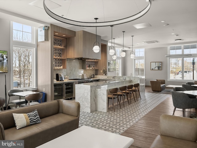 kitchen with pendant lighting, tasteful backsplash, a breakfast bar area, wine cooler, and light stone counters