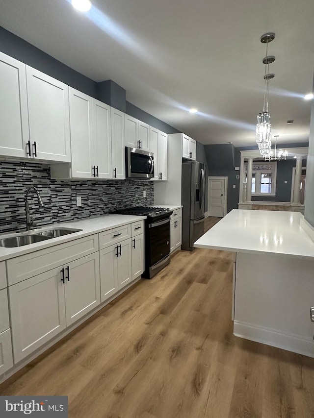 kitchen with appliances with stainless steel finishes, white cabinetry, decorative light fixtures, and sink