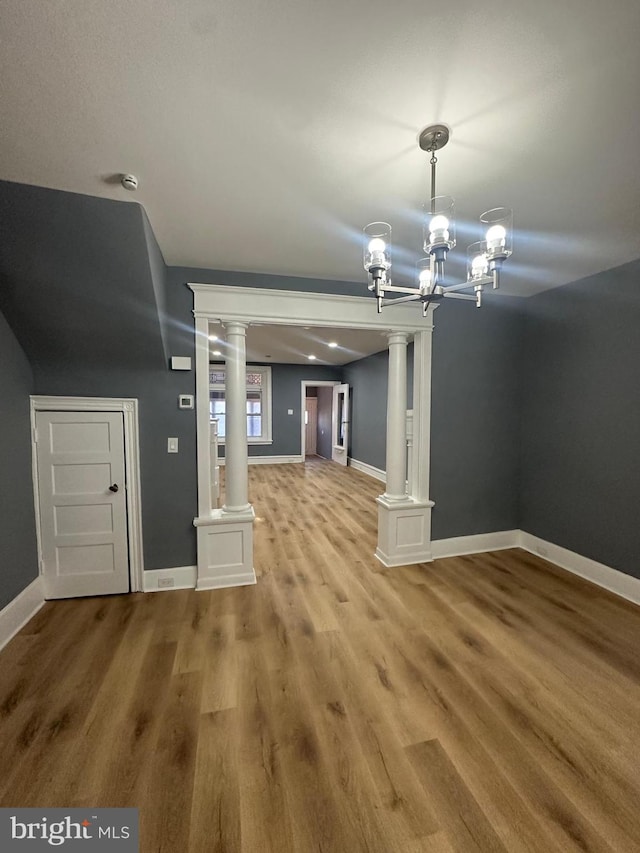 unfurnished living room with an inviting chandelier, decorative columns, and wood-type flooring