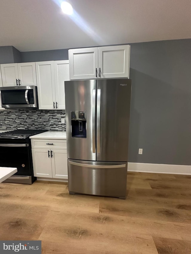 kitchen featuring decorative backsplash, white cabinetry, light wood-type flooring, and appliances with stainless steel finishes