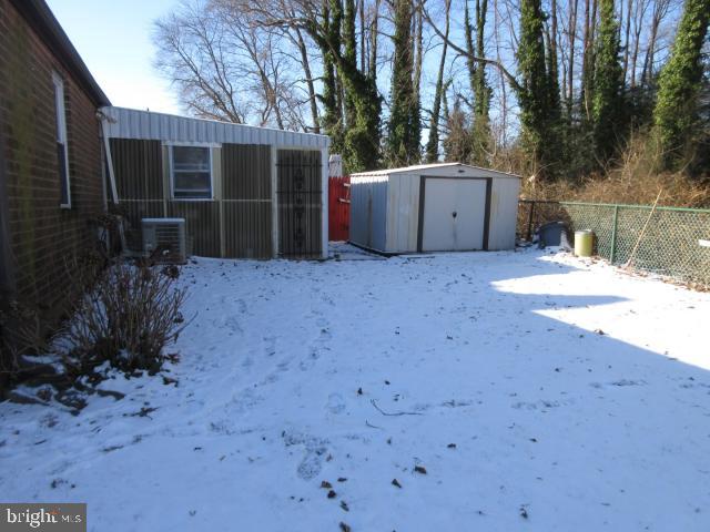 yard layered in snow featuring a shed and central AC unit