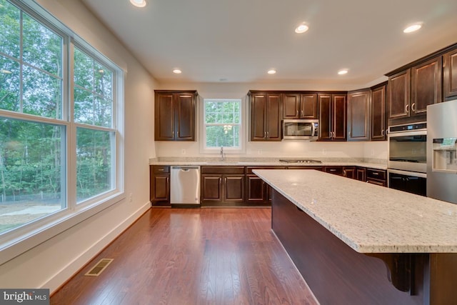 kitchen featuring dark brown cabinetry, dark hardwood / wood-style flooring, stainless steel appliances, sink, and a breakfast bar area