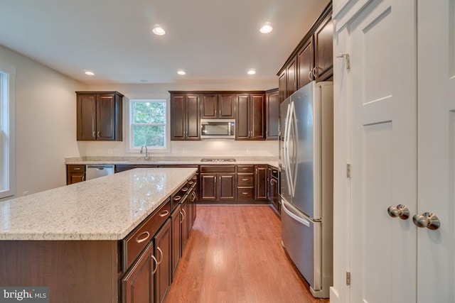 kitchen featuring light stone countertops, appliances with stainless steel finishes, dark brown cabinets, and a kitchen island