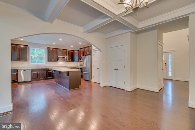 kitchen featuring stainless steel appliances, beam ceiling, ornamental molding, and a center island