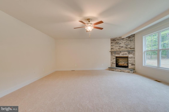 unfurnished living room with ceiling fan, carpet floors, and a stone fireplace