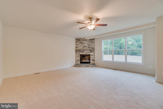 unfurnished living room with ceiling fan, carpet floors, and a stone fireplace