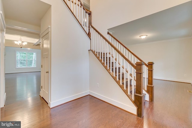 staircase featuring hardwood / wood-style floors, ornamental molding, and an inviting chandelier