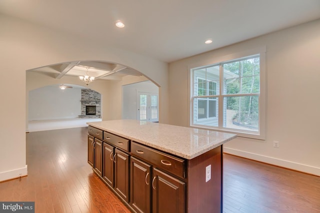 kitchen with a kitchen island, beamed ceiling, coffered ceiling, dark brown cabinetry, and a stone fireplace